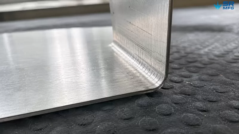 Macro view of tool marks and pressure impressions left on 1.2mm polished stainless steel sheet after press brake bending