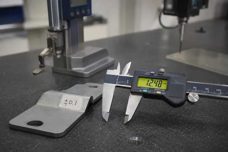 Digital caliper measuring a sheet metal bracket on a granite surface plate in a metrology lab