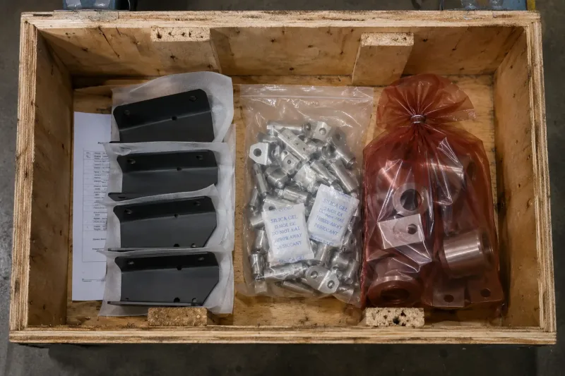 Open shipping crate showing three packaging methods: PE film for coated parts, sealed bags with desiccants for plated parts, and VCI bags for bare metal
