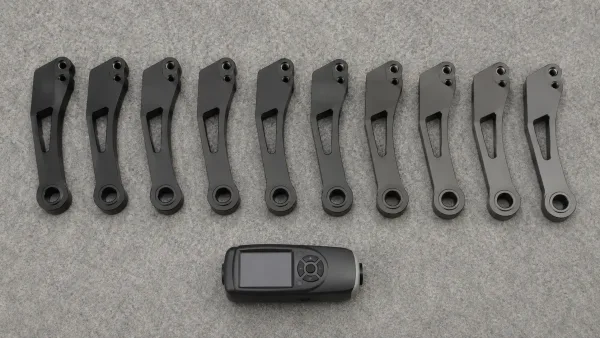 Row of identical black anodized aluminum parts showing gradual color variation from deep black to grey across a production lot