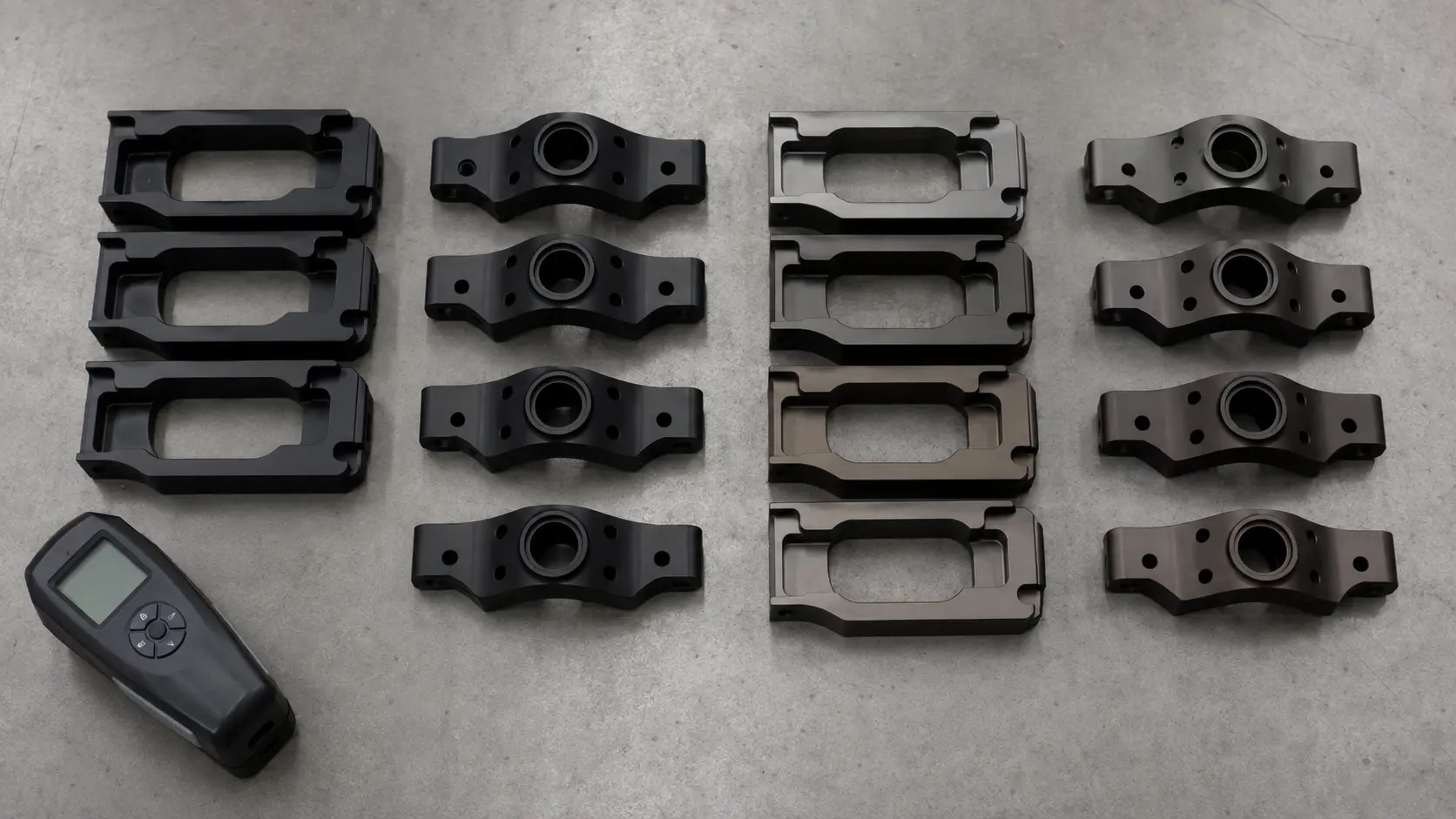 Black anodized aluminum parts arranged on an inspection surface next to color variation samples showing inconsistent black tones